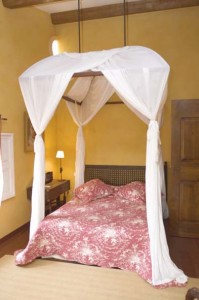 Ambiance romantique pour cette chambre avec lit à baldaquin, d’où s’échappe un beau drapé de tissu retenu dans le haut par des embrasses assorties. 